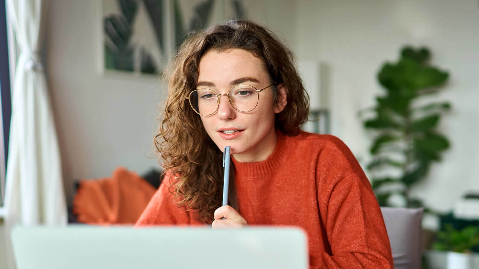 a student holds a pen and looks at her open laptop as she studies for the ACT