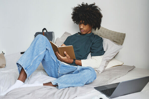 a student studies from a notebook while laying on his bed
